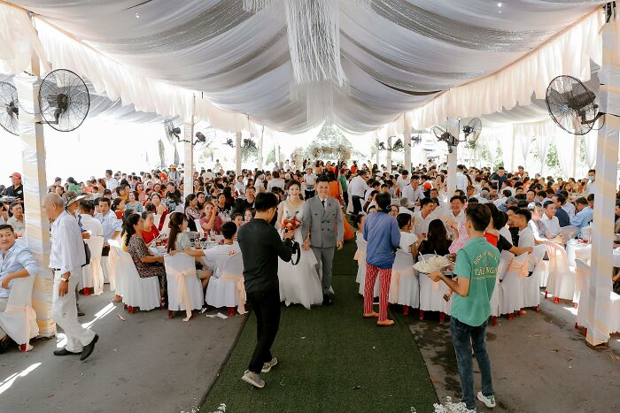 Large gathering in a decorated tent with people seated at tables, celebrating with festive decorations all around.