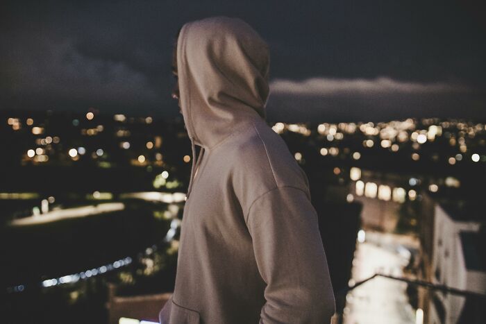 Person in a hooded sweatshirt overlooking city lights at night, challenging common stereotypes.