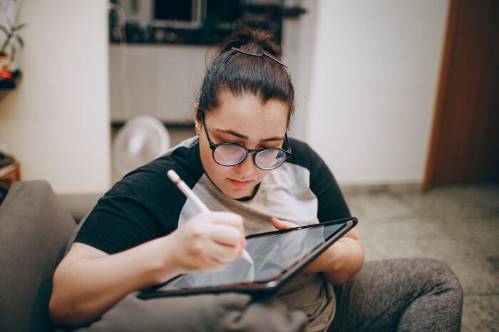 A person using a tablet at home, focusing intently on digital drawing.