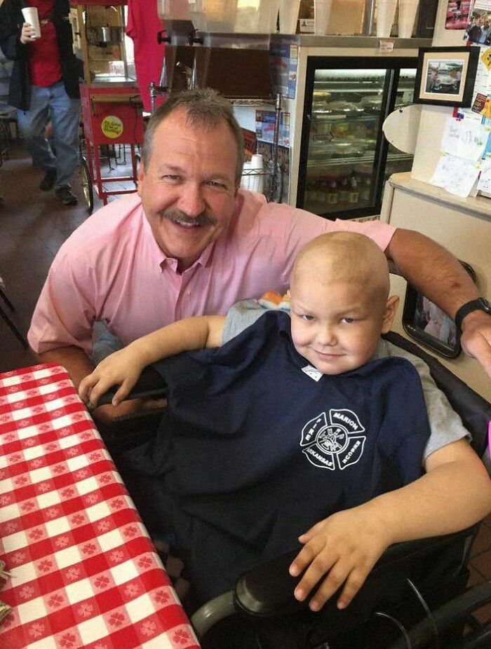 Man in a pink shirt and a smiling child in a wheelchair, sharing a positive and uplifting moment at a checkered table.