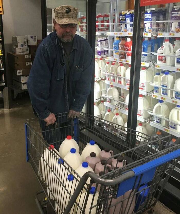 Man in denim jacket and hat with a cart full of milk jugs in a grocery store, embodying a positive moment.