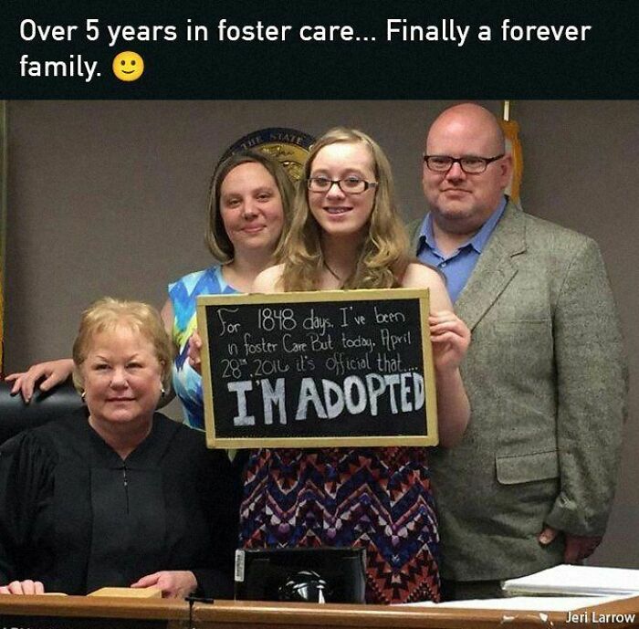 Young girl holds adoption sign with family, bringing positivity and hope after years in foster care.