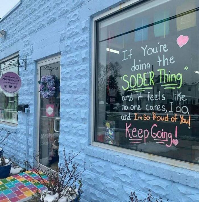 Blue building with a colorful window sign, spreading positive and uplifting messages about sobriety and encouragement.