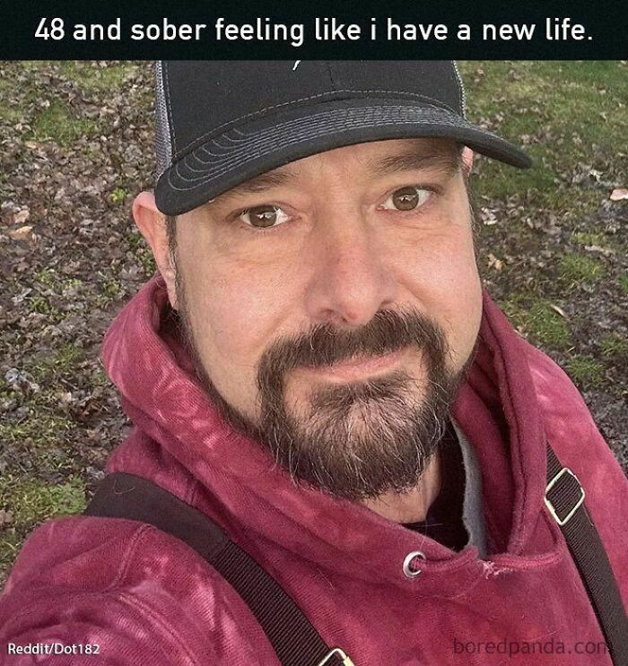 Man in a red hoodie and cap smiling, embodying positive and uplifting vibes in a park setting.