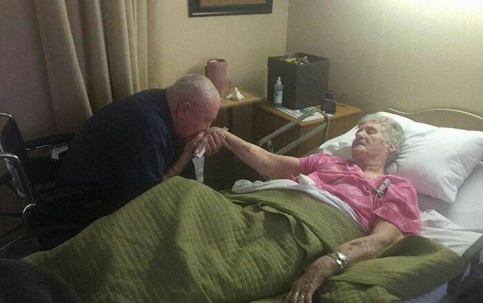 Elderly man kisses woman’s hand in a caring and uplifting hospital setting, creating a positive and heartfelt moment.