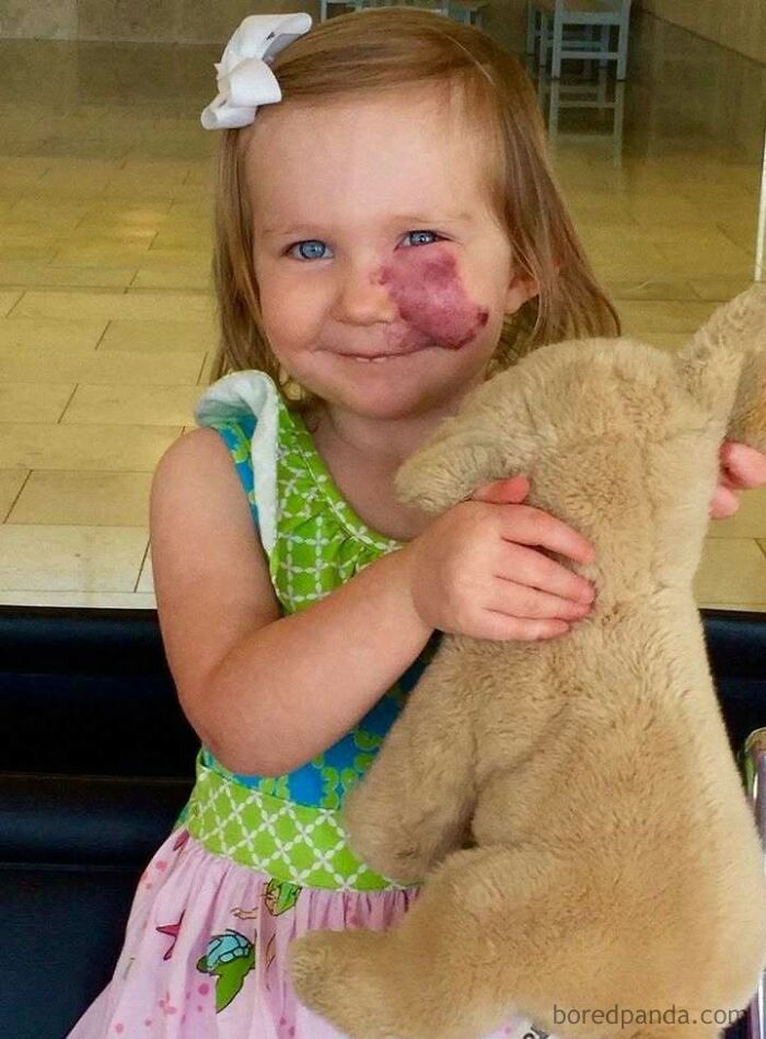 A smiling child holding a teddy bear, embodying positivity and upliftment, with a cute bow in her hair.