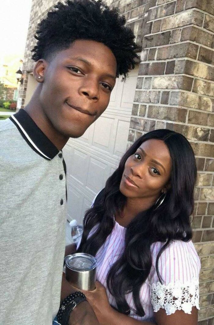 Two people smiling outside near a brick wall, holding a cup, creating a positive and uplifting vibe.