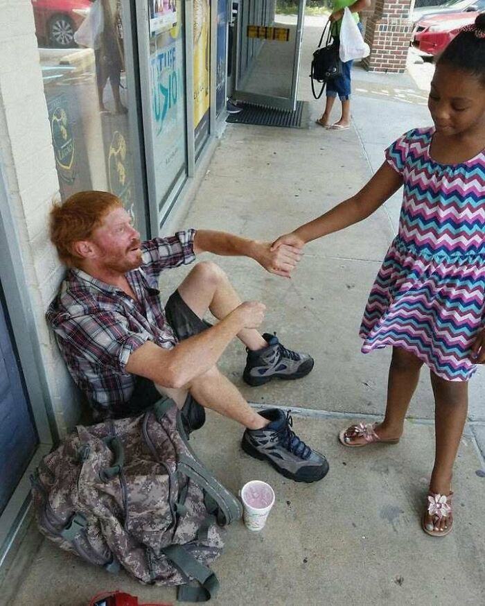 Man sitting on sidewalk and shaking hands with a young girl, creating an uplifting and positive moment.