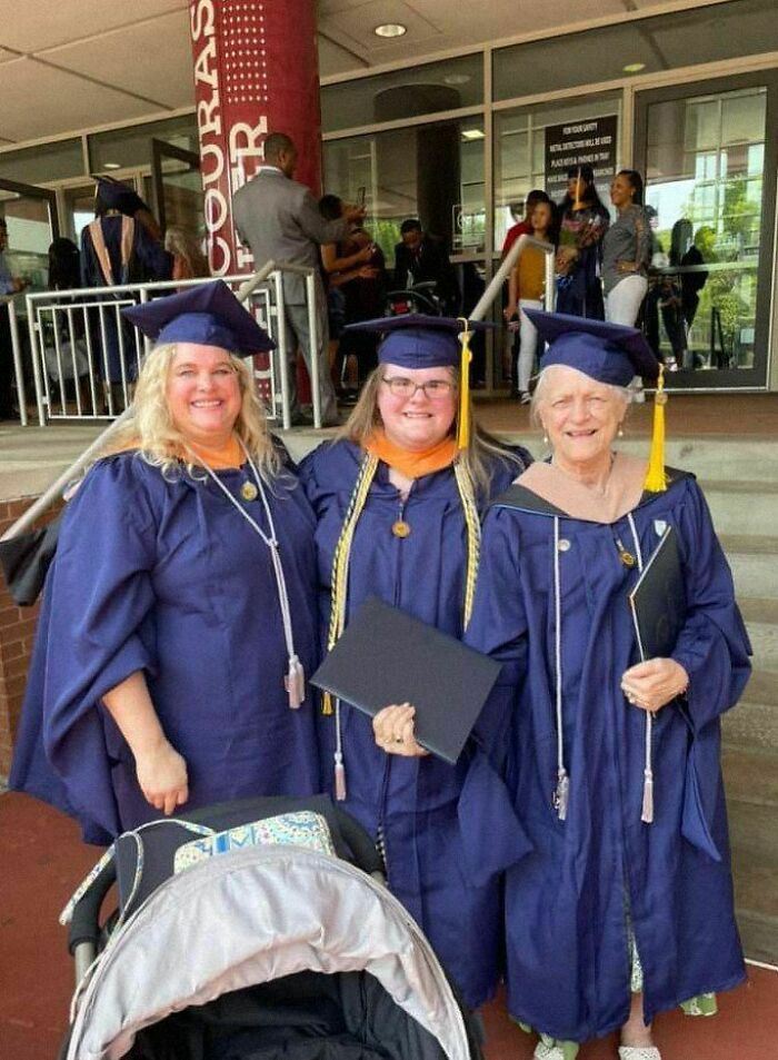 Three graduates in navy gowns and caps smiling, holding diplomas. Positive and uplifting scene outside a ceremony.