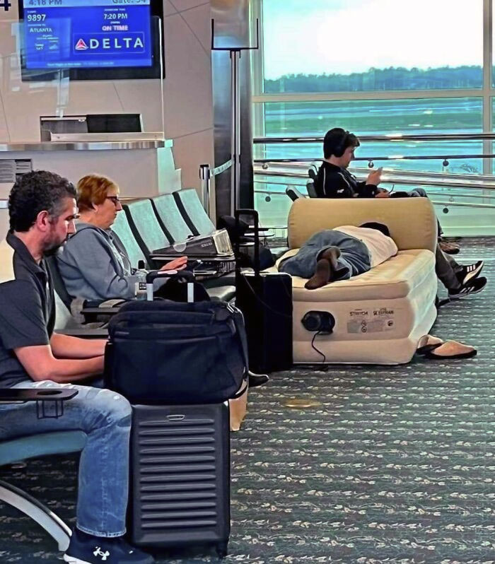 Airport seating area with travelers; one person is lying on an inflatable mattress.
