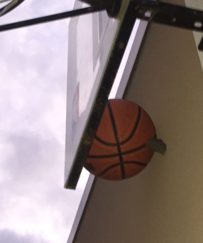 Basketball improbably wedged between hoop and backboard, showcasing an unbelievable moment captured in a photo.