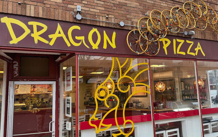Pizza place exterior with a dragon mural and bicycles above the door.