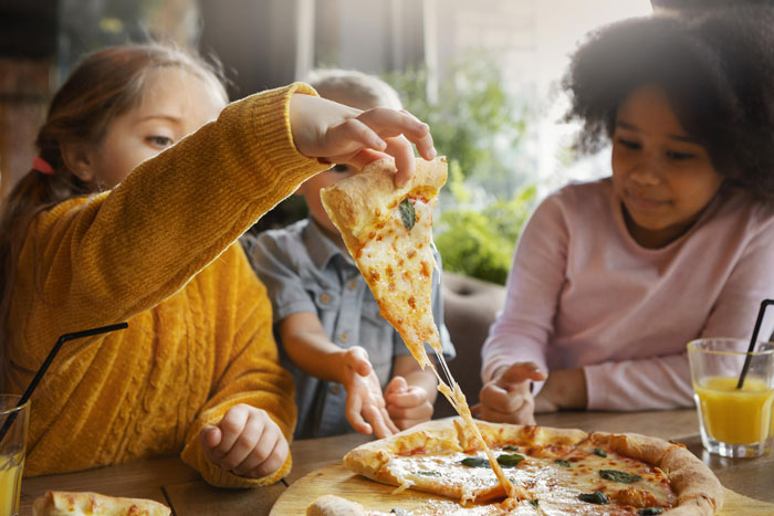 Children enjoying pizza at a restaurant, illustrating the issue of unruly kids affecting dining experiences.