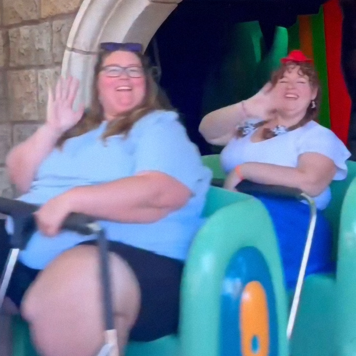 Two plus-size park hoppers enjoying a ride, smiling and waving with empowerment. Two plus-size park hoppers enjoying a ride, smiling and waving with empowerment.