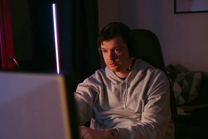 Person in a hoodie focused intently on a computer screen, dimly lit room, possibly participating in an online eating competition.