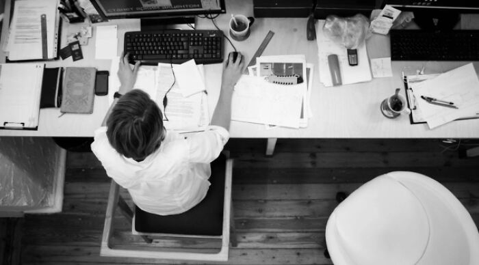Person at a desk working on dilemmas, surrounded by papers and stationery, typing on a keyboard.