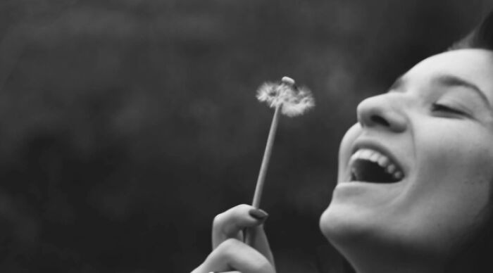 Smiling woman with dandelion, representing choice in a black-and-white setting.