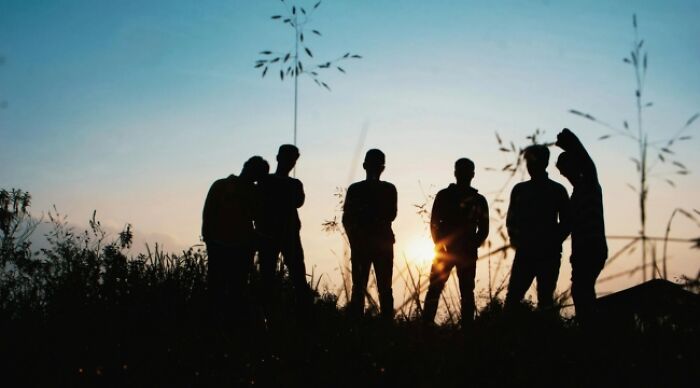 Silhouettes of people at sunset in a field, pondering dilemmas.