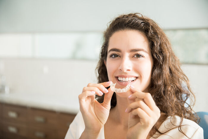 A person smiling while holding a dental aligner, unrelated to unexpected cat gifts.