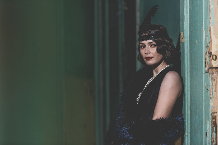 Woman in vintage attire, with pearls and feather headband, evoking gradually disappeared styles from the past.