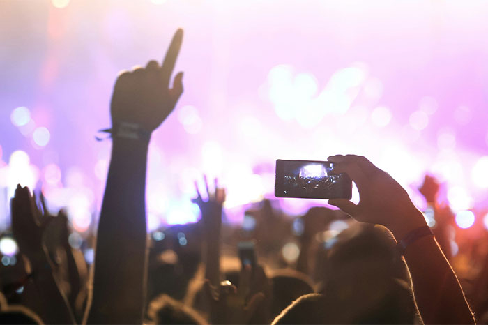 A crowd at a concert, with someone taking a photo using a smartphone.