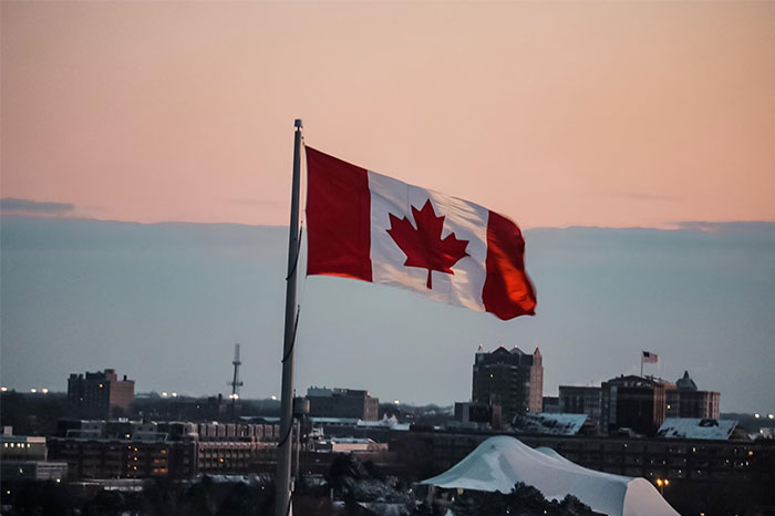 Canadian flag waving over cityscape at sunset, with buildings in the background.