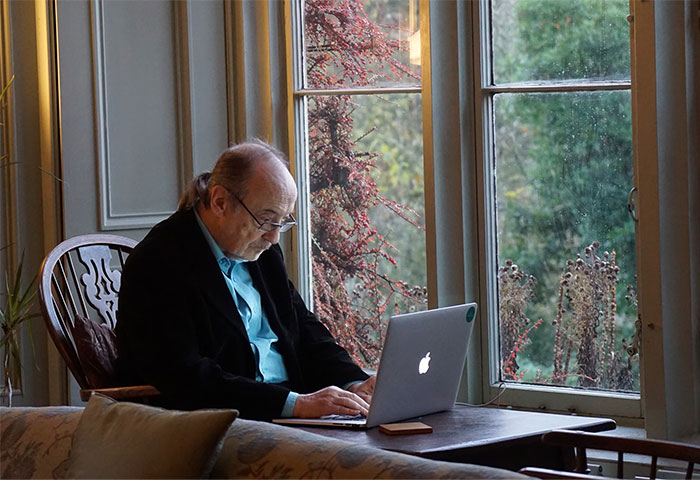 Elderly man in glasses typing on a laptop by a window, representing accidental social media posts.