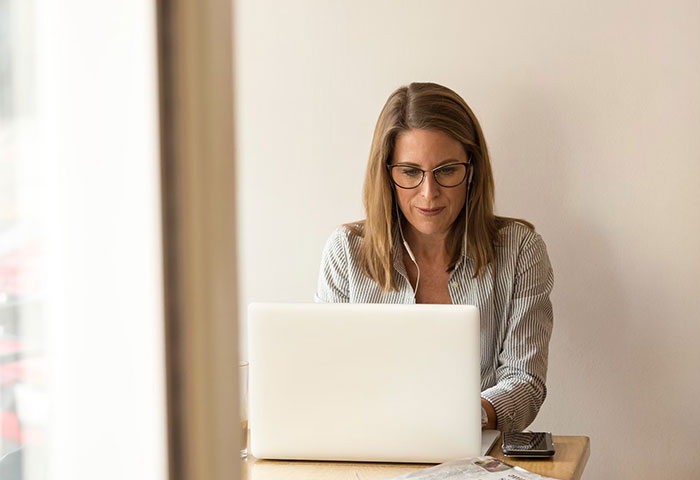 Woman using a laptop at a desk, focused on accidental social media posts while wearing glasses in a casual setting.