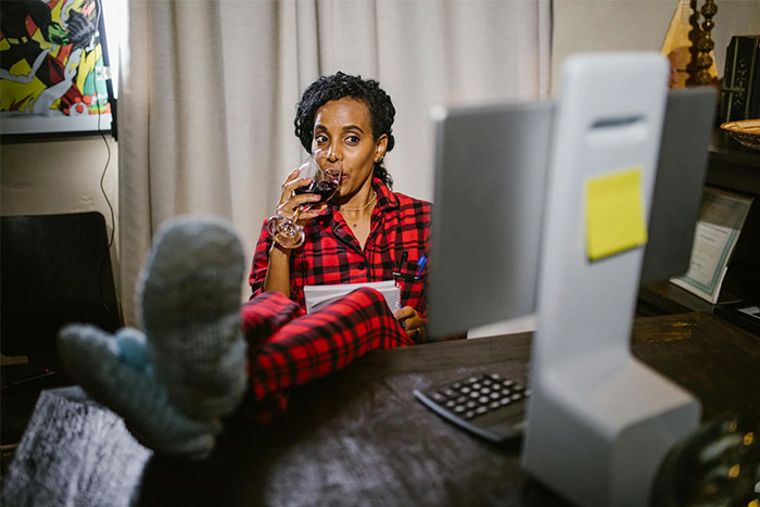 Person in red pajamas, sipping wine, feet up, at desk with computer, reflecting a casual social media moment.