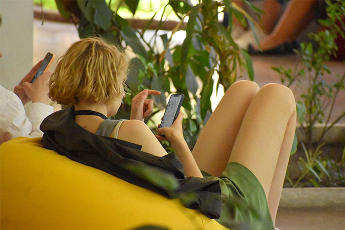 A person in a green dress lounging and scrolling through social media on their phone, outdoors.