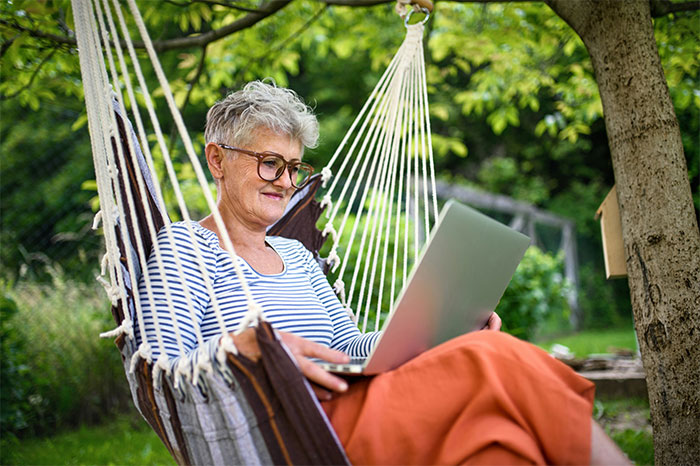 Woman in hammock using a laptop outdoors, working or browsing social media on a sunny day.