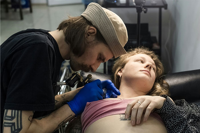 Tattoo artist working on a woman's tattoo, focusing intently, exemplifying social media mishaps during personal moments.