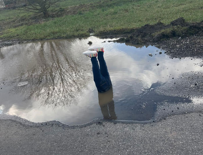 Legs sticking out of a pothole prank, drawing attention to road hazards.