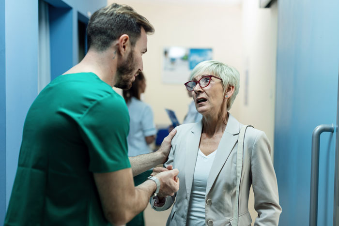 Medical staff talking to a concerned older woman in a hospital corridor.