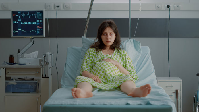 Pregnant woman resting in hospital bed after a fall, with medical equipment nearby.