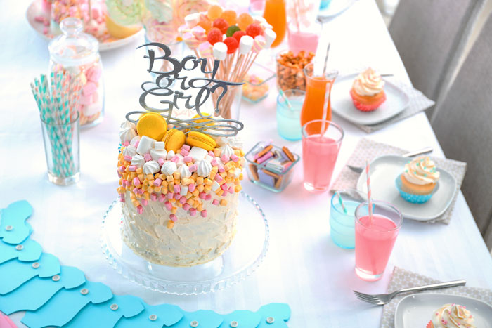 Gender reveal party setup with colorful cake and drinks.