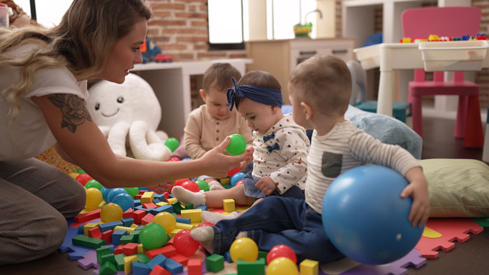 Mother engaging in childcare, playing with toddlers surrounded by colorful toys.