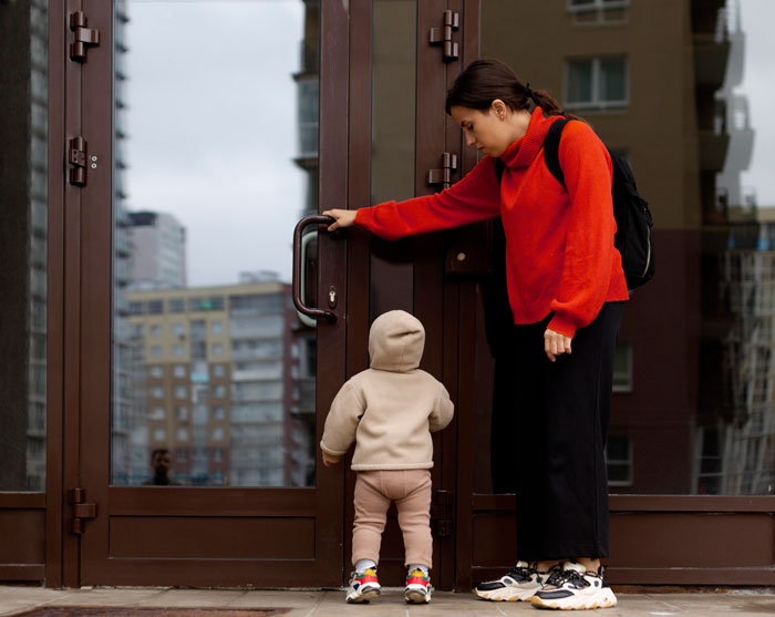 A woman in a red sweater and child at a door, relevant to pregnant-wife-childcare.