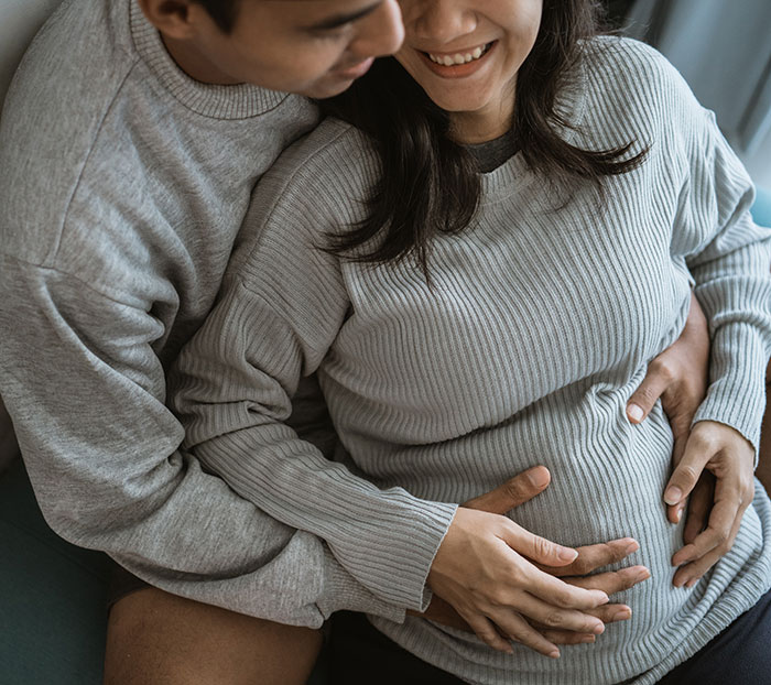 Couple embracing with smiles; man supports woman's stomach, sharing a tender moment. Couple embracing with smiles; man supports woman's stomach, sharing a tender moment.