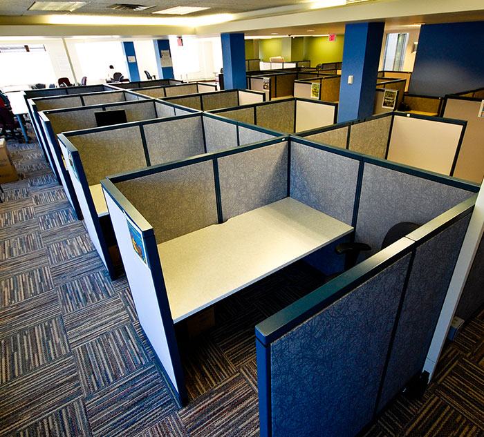 Rows of empty office cubicles with gray partition walls, offering a glimpse into modern workspace design.