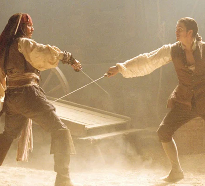 Two people sword fighting in a dimly lit room, wearing period clothing, as an opportunity to learn new fencing techniques.