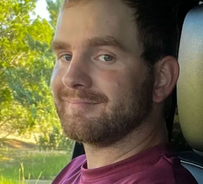 Smiling man in a maroon shirt inside a vehicle, surrounded by greenery, opportunity to learn something new today.