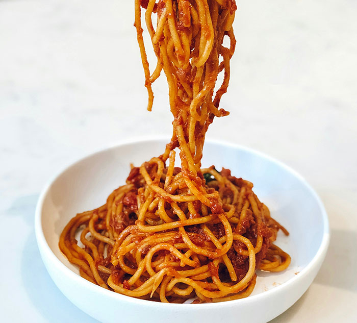 A plate of spaghetti with tomato sauce, captured mid-serving, showcasing a delicious pasta dish.