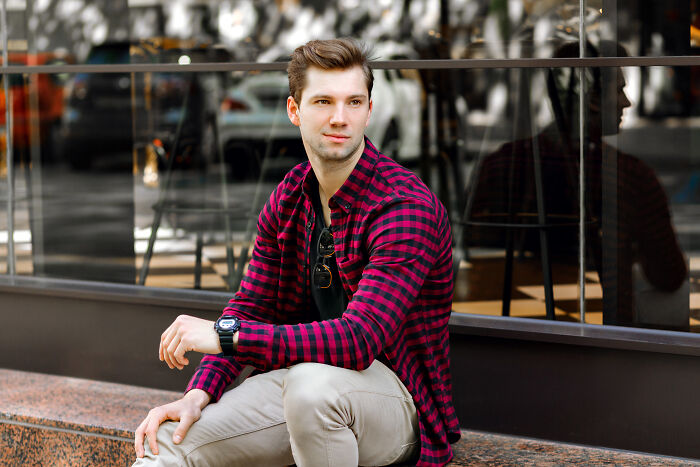 Man in checkered shirt sitting outdoors, showcasing pretty privilege benefits in urban setting.