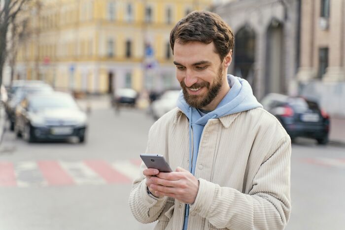 Man smiling while using his phone, illustrating how "pretty privilege" can favor men in everyday situations.