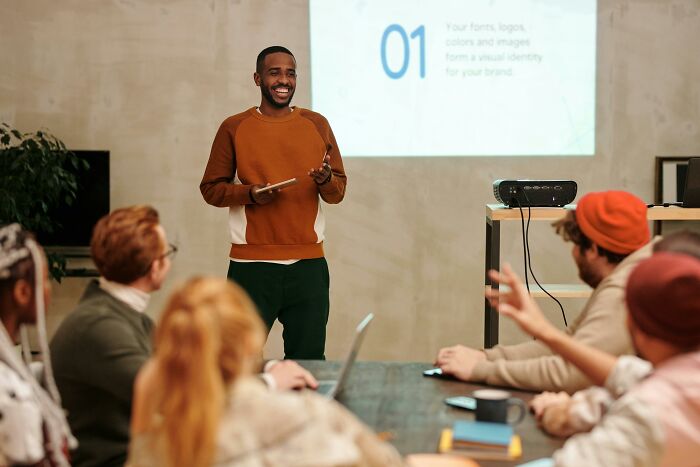 Man presenting to colleagues, showcasing "pretty privilege" in action with diverse people interacting in a meeting room.