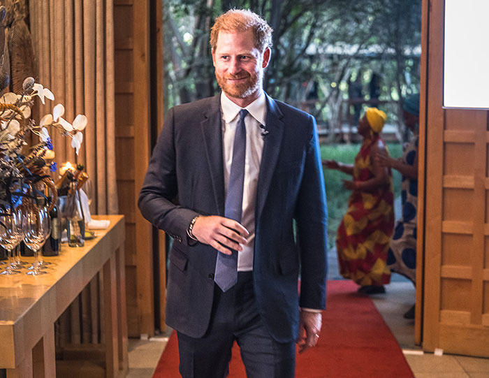 Man in a suit walking on a red carpet, near a decorated table, outdoors.