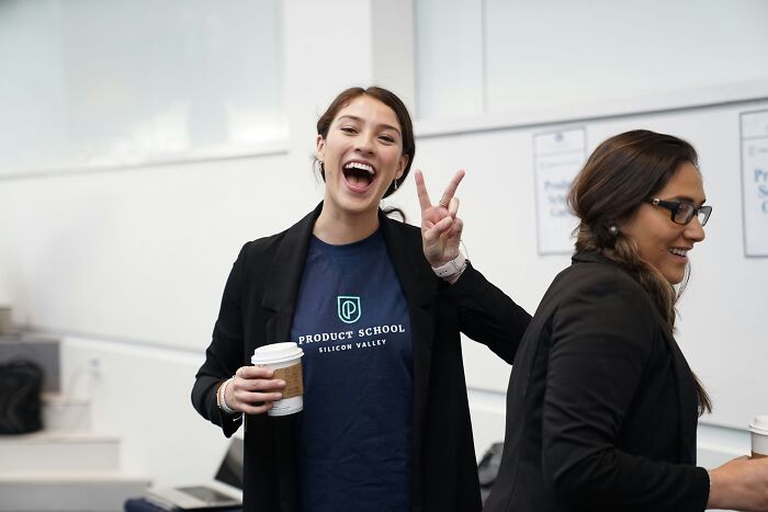 "Smiling woman in a classroom making a peace sign, possibly a sign of intelligence."