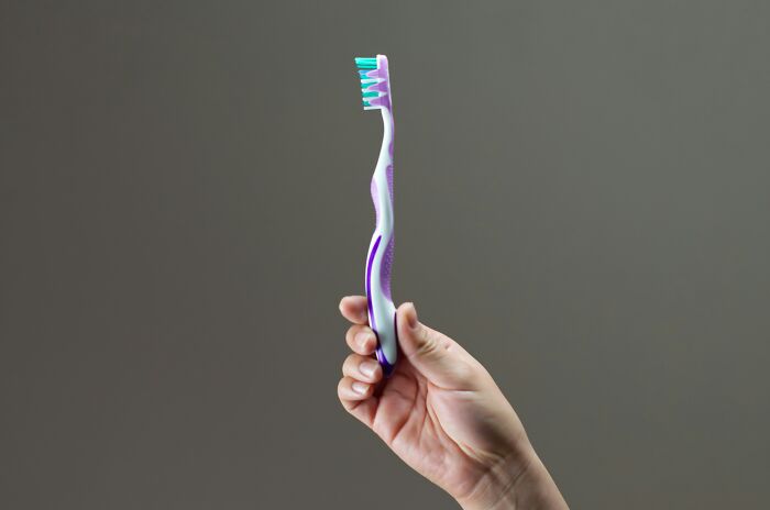 Hand holding a toothbrush, potentially used for a purpose other than brushing teeth.