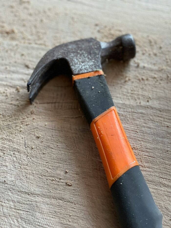 Hammer with a black and orange handle lying on wood, used differently than intended purpose.